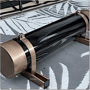 Black telescope tube with bronze end caps secured by metal rings on a mounting, lying on a patterned outdoor rug