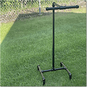 Black adjustable-height stand with a wheeled four-point base on a grassy lawn; a horizontal bar at the top with handles.